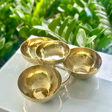 Load image into Gallery viewer, Set of four gold bowls on a white surface with green foliage in the background
